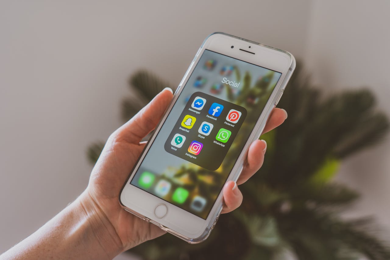 Close-up of a hand holding a smartphone displaying popular social media apps.
